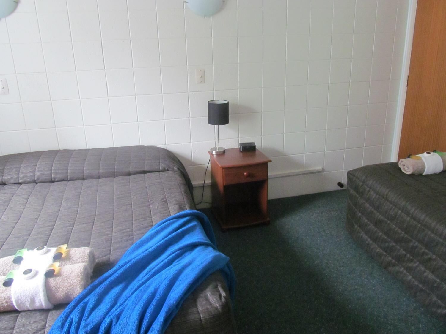 Habitación de hotel con dos camas, una mesita de noche con lámpara y un enchufe en la pared.