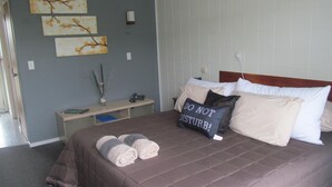 A neatly made bed with a brown bedspread, a bedside table with a lamp, and three wall-mounted artworks. - Parkview Motel (Dargaville)
