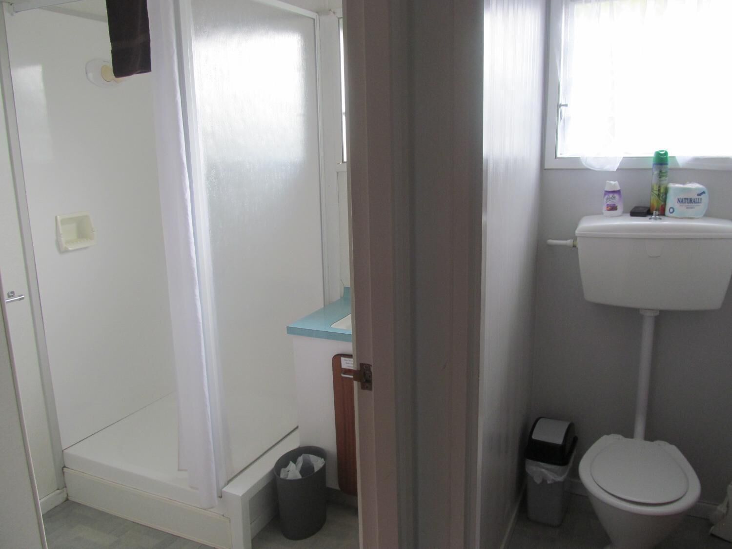 A bathroom with a toilet, a trash bin, and a window with a curtain.