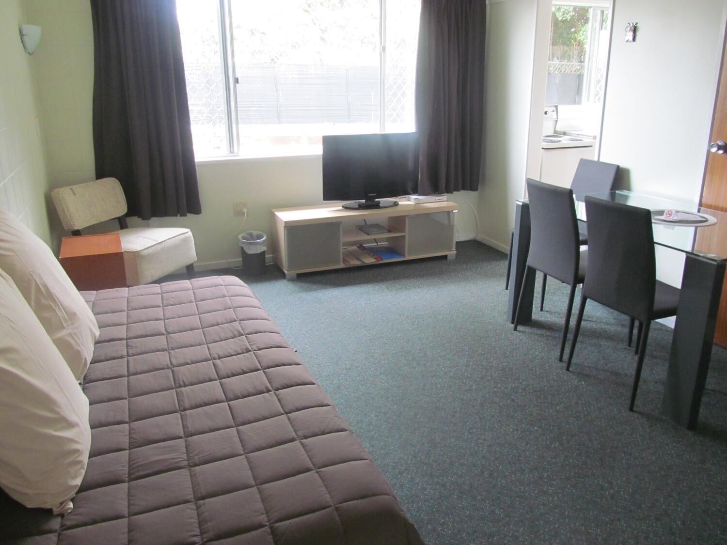 Une chambre d’hôtel comprenant un lit, un bureau avec une chaise, une télévision et une fenêtre avec des rideaux.