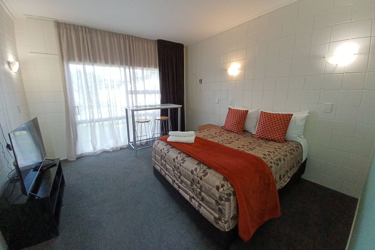 A hotel room with a bed, a desk with two chairs, a television, and a window with curtains.