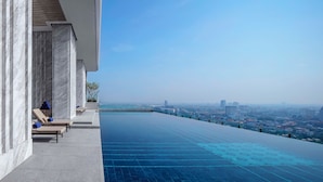 Une piscine à débordement située sur le toit, offrant une vue sur la ville, ainsi que des chaises longues et une architecture moderne.
