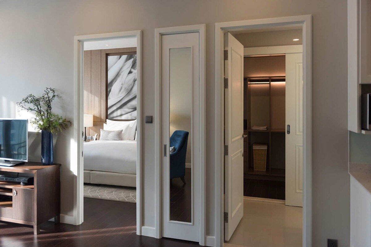 Een hotelkamer met een bed, een televisie, een vaas met planten en een badkamer zichtbaar door een geopende deur.