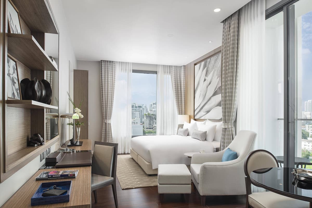 Een moderne hotelkamer met een groot bed, een bureau met stoel, een bank en een glazen tafel.