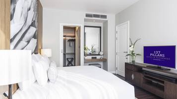A modern hotel room with a large bed, a TV, a walk-in closet, and a bathroom visible through an open door.