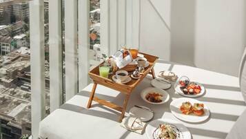 A balcony with a wooden tray table set with breakfast items, including fruits, pastries, and beverages.