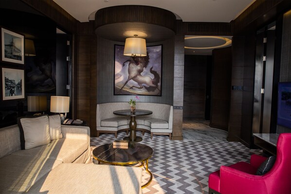 A modern lobby with a sofa, armchairs, a round table, a lamp, and a large framed artwork. - 137 Pillars Suites Bangkok (Bangkok)