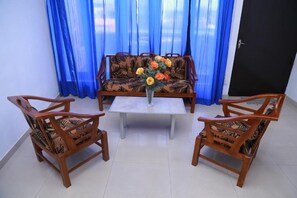 A room with a sofa set, two wooden chairs, a coffee table, and a vase with flowers. - Villa 142 (Mount Lavinia)