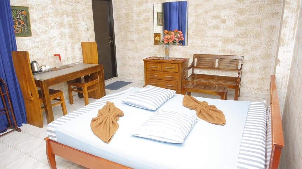 Una habitación de hotel con una cama, un escritorio, una silla, un aparador y un espejo.
