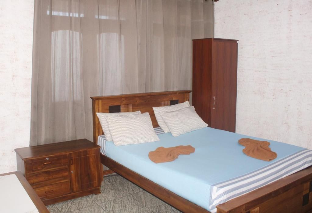 A bedroom with a wooden bed, a nightstand, a wardrobe, and a window with sheer curtains.
