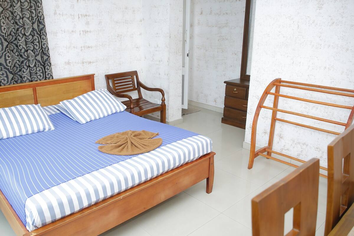 A neatly made bed with striped bedding, a wooden headboard, and a towel on the bed. There is a wooden chair and a wooden stool in the room.