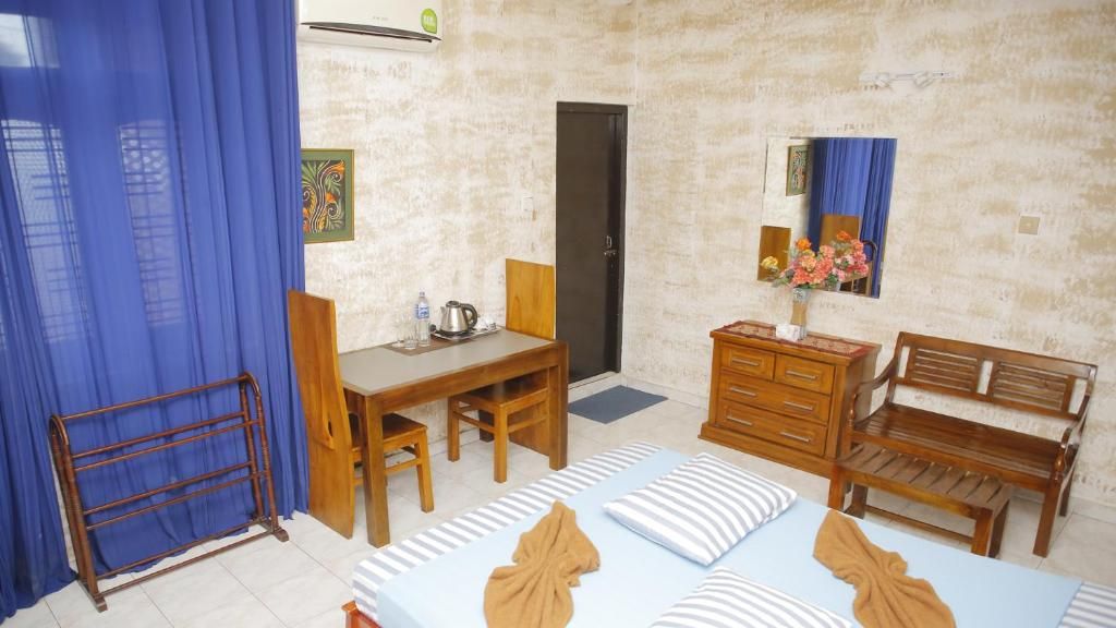 A hotel room with a bed, a desk, a chair, a dresser, and a bench.