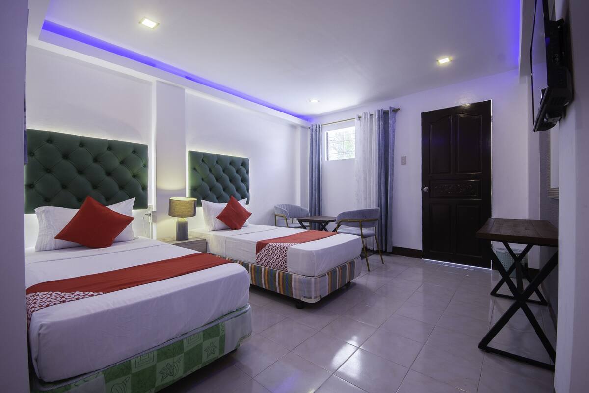 Une chambre d’hôtel avec deux lits, un bureau, une chaise et un téléviseur.