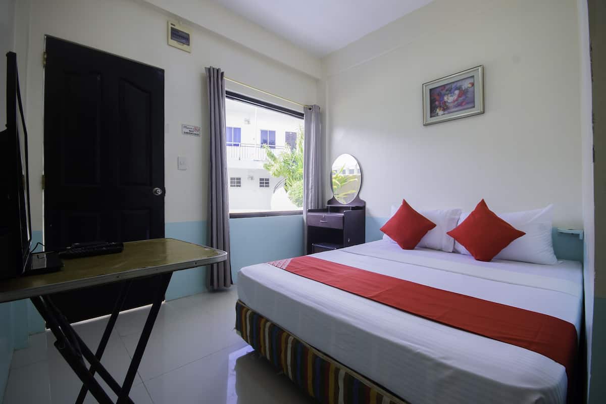 Une chambre d’hôtel avec un lit, un bureau, une télévision, une fenêtre avec des rideaux et un tableau au mur.