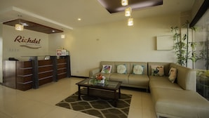 A reception area with a reception desk, a sofa, a coffee table, and a large window with plants. - OYO 725 Richdel Resort Hotel (Lapu-Lapu)