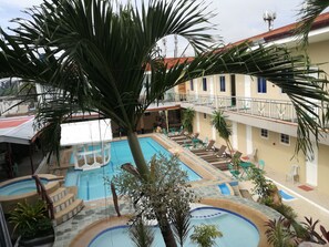 Uma área de piscina com vários níveis, palmeiras e espreguiçadeiras.