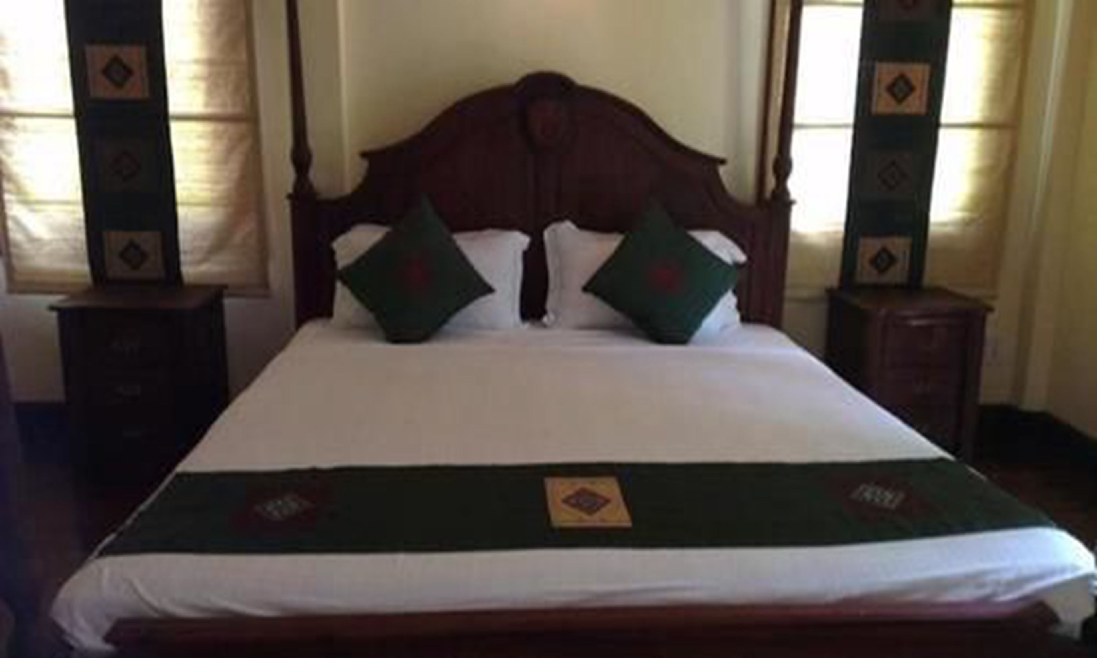 A neatly made bed with a wooden headboard, two pillows, and a green throw blanket.
