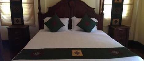 A neatly made bed with a wooden headboard, two pillows, and a green throw blanket.