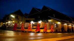 Monks in orange robes walking in front of a building with a sign that reads "BOUKHAM CHANTHAS GUEST HOUSE". - Nocknoy Lanexang Guesthouse (Luang Prabang)