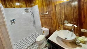 A bathroom with a wooden wall, a white sink, a toilet, and a shower. - Nocknoy Lanexang Guesthouse (Luang Prabang)