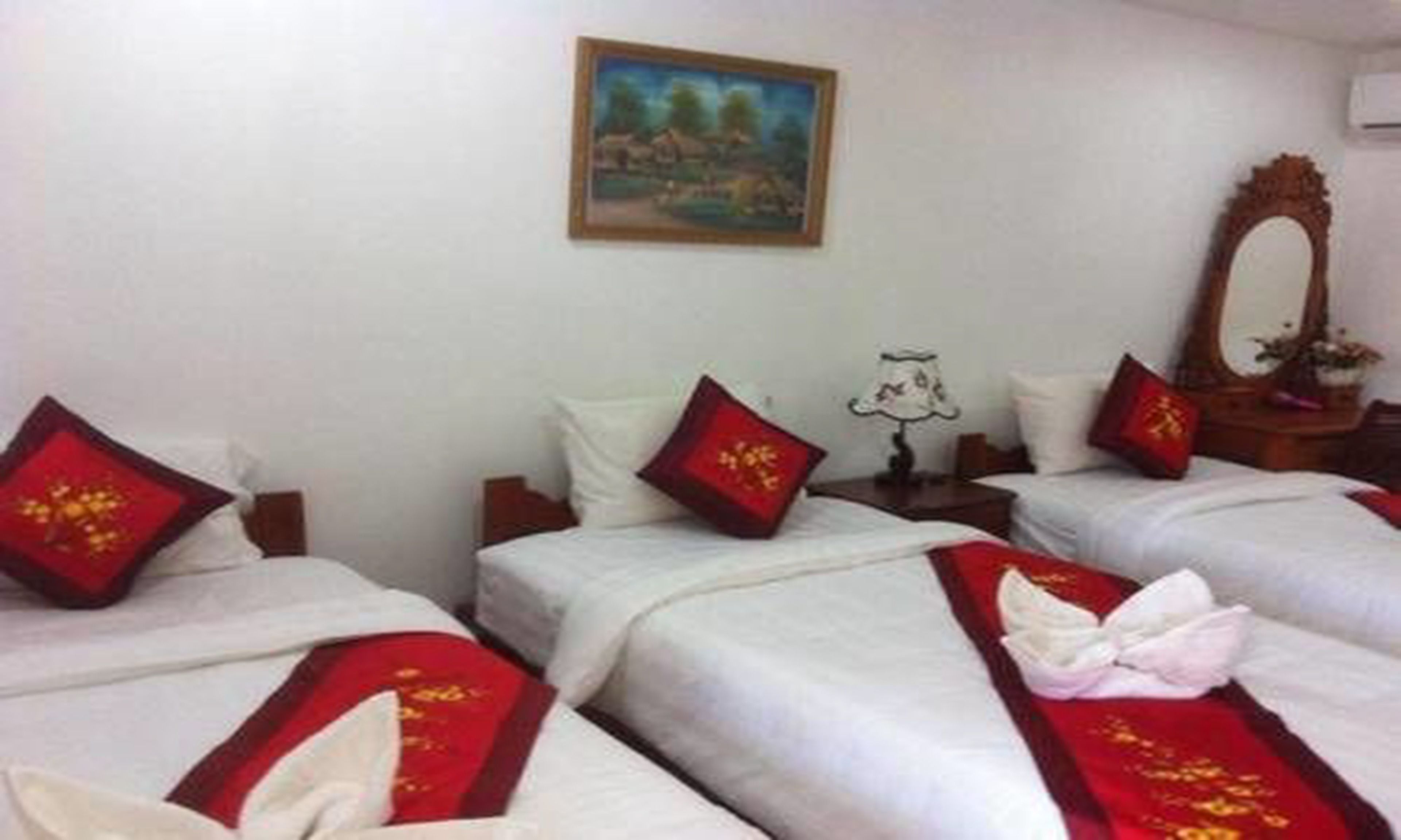 A hotel room with two beds, each with red and white bedding, a painting on the wall, and a mirror on the dresser.