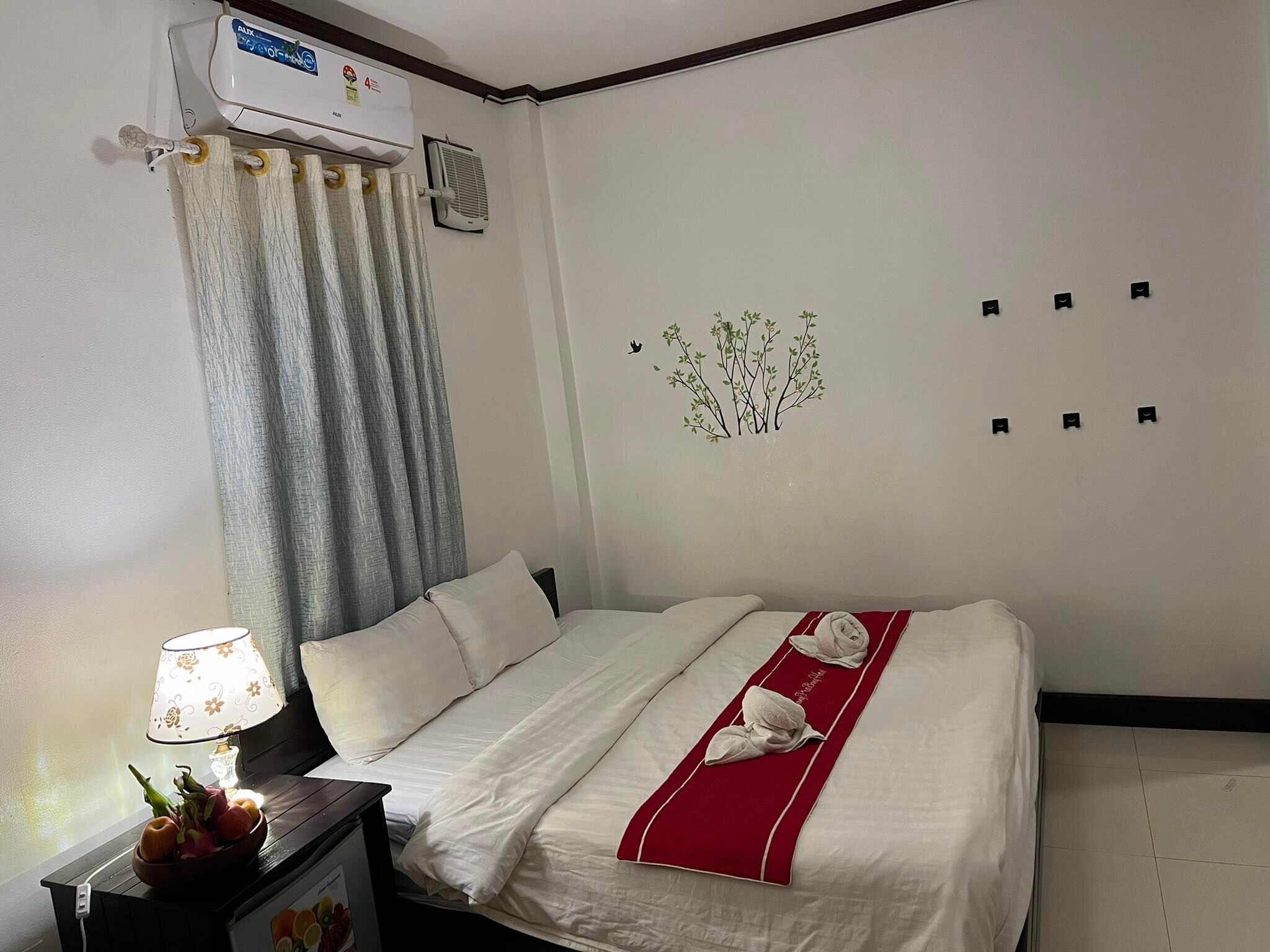 Een hotelkamer met een bed, een nachtkastje met een lamp, een schaal fruit en een airconditioner aan de muur.