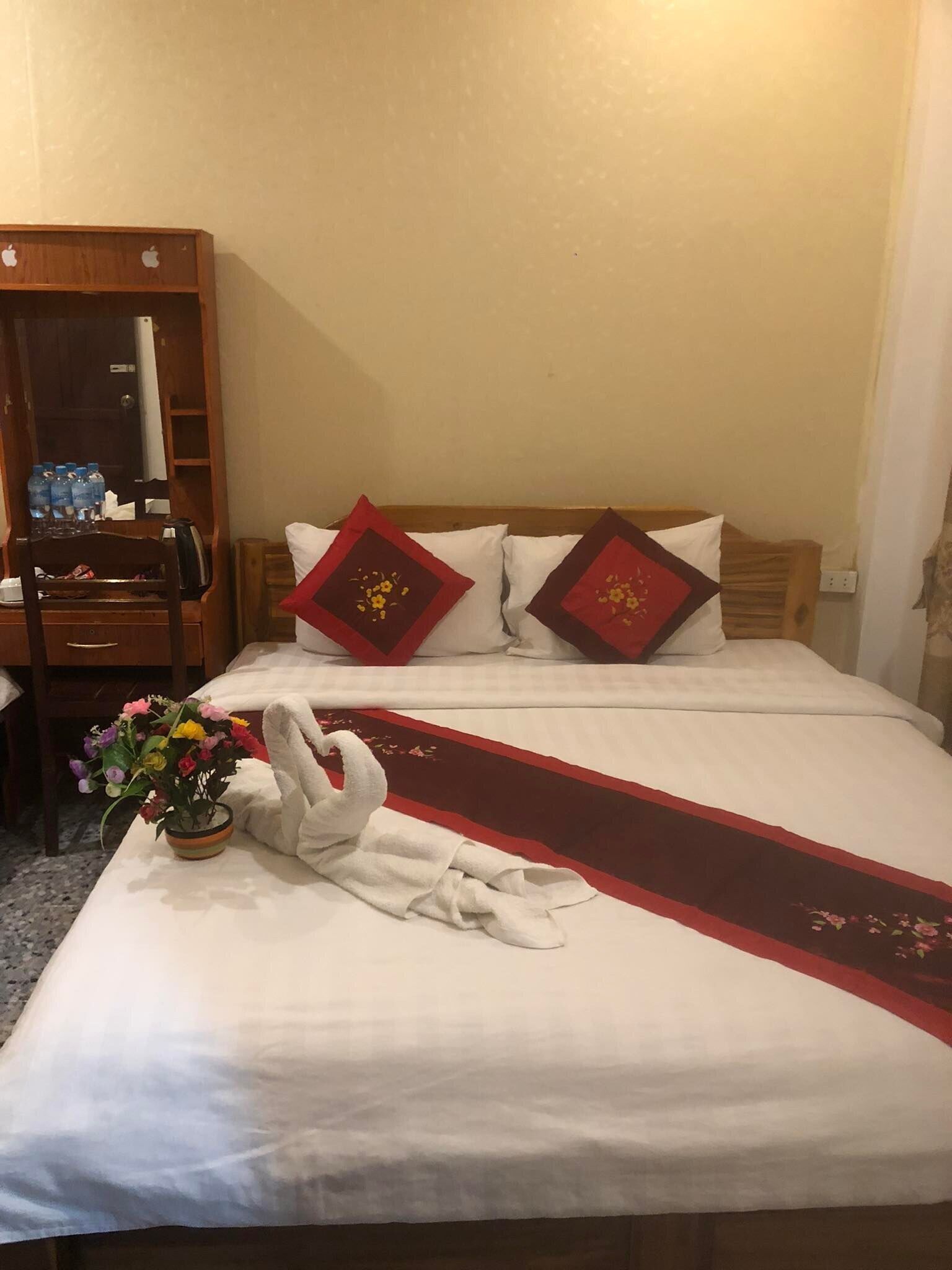 Siisti hotellihuone, jossa on huolitellusti pedattu sänky, puinen työpöytä, jossa on peili, ja maljakko täynnä kukkia.