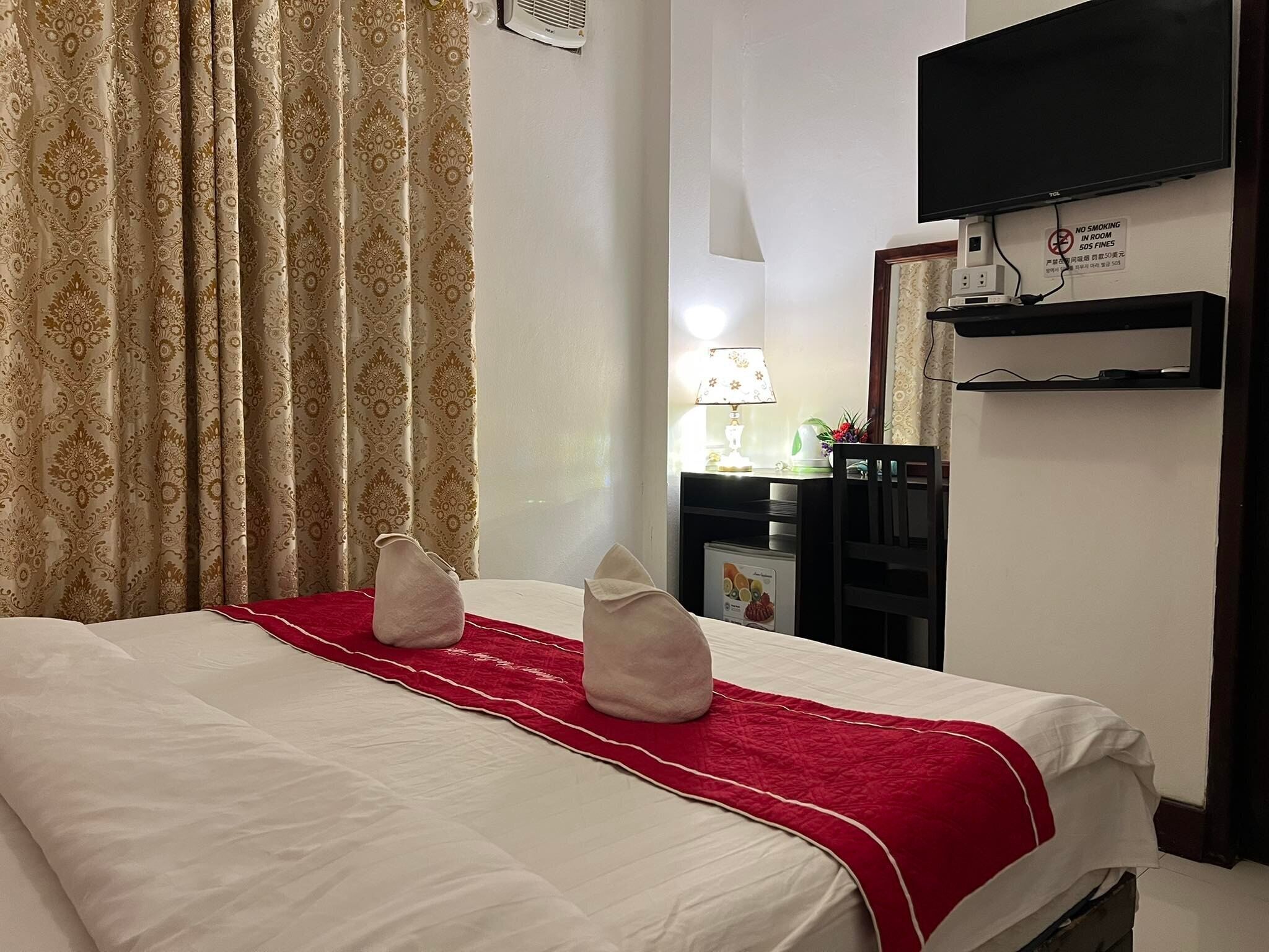 Ein Hotelzimmer mit einem Bett, einem an der Wand befestigten Fernseher, einem Schreibtisch mit Lampe und einem Sessel.