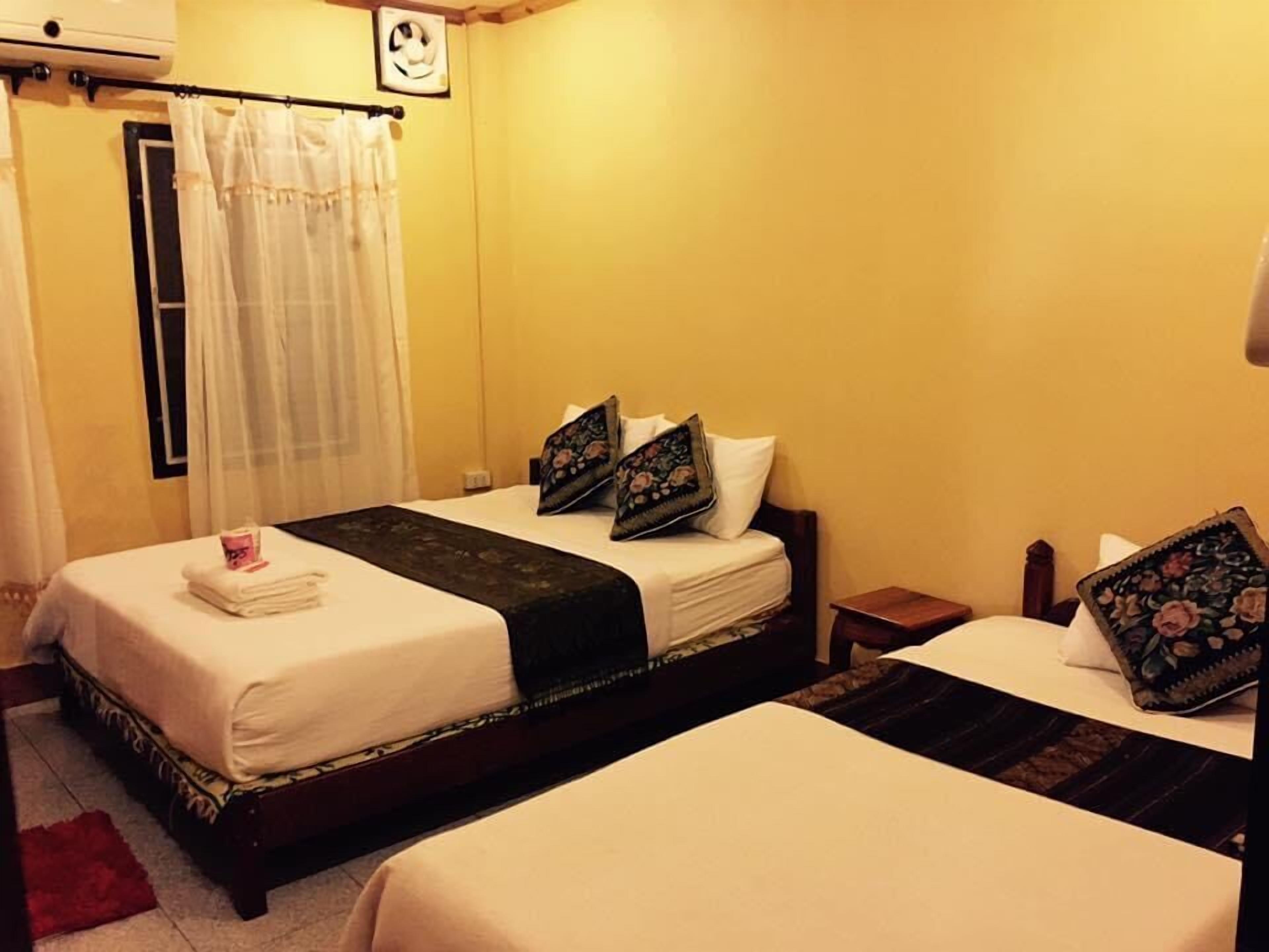 A hotel room with two beds, a bedside table, a nightstand, a window with a curtain, and a wall-mounted air conditioner.