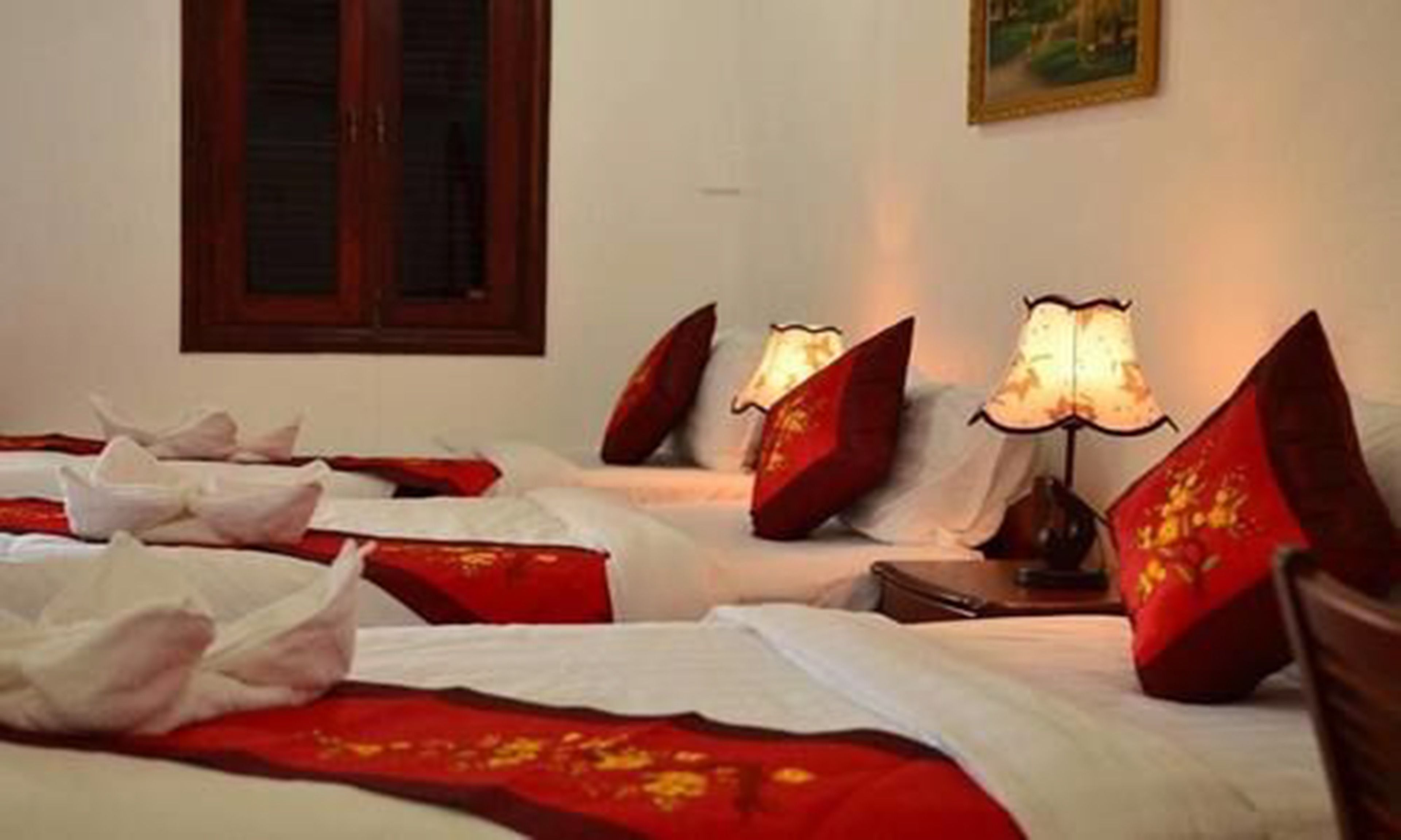 Une chambre d’hôtel avec deux lits, une literie rouge, des oreillers blancs et une table de chevet avec une lampe.