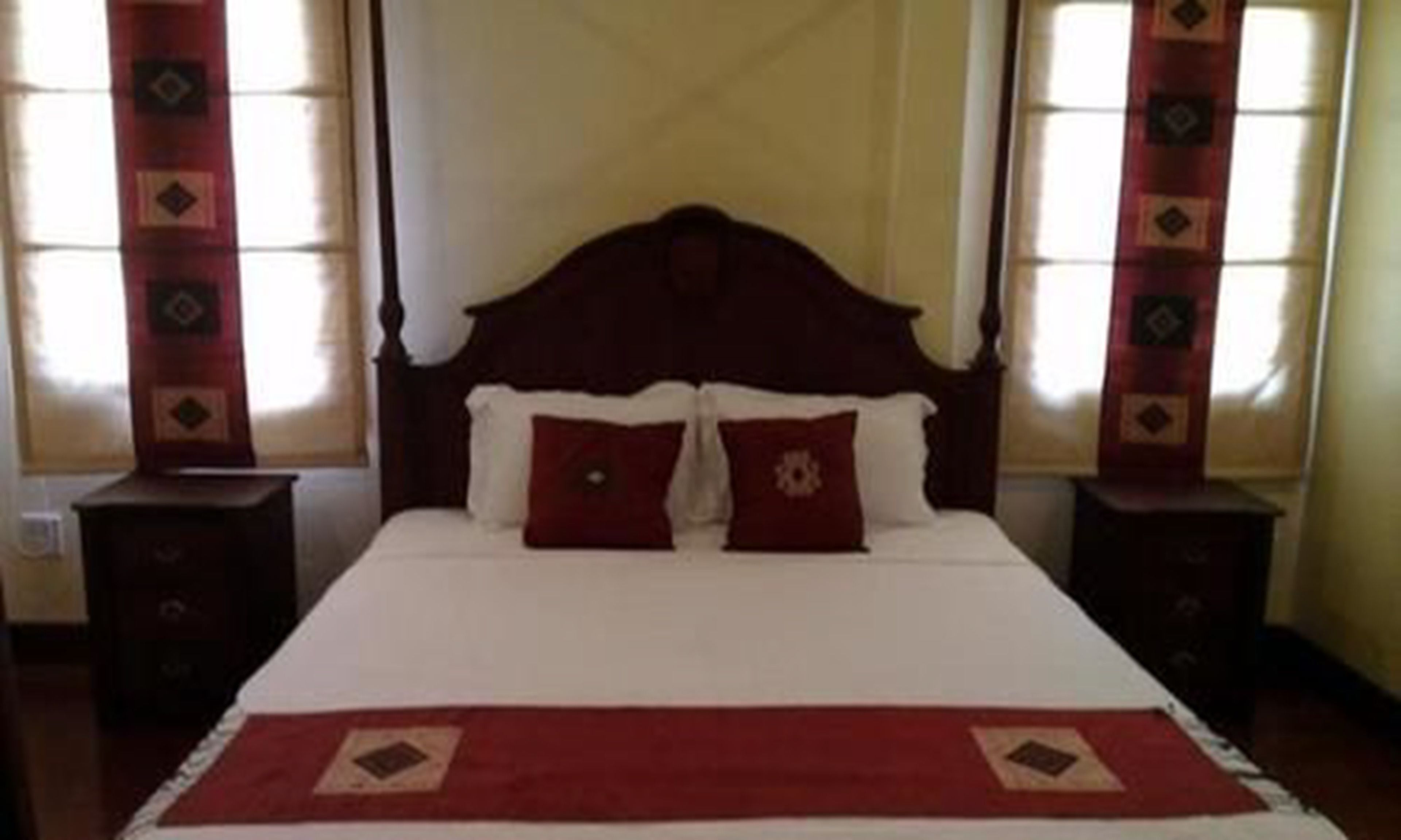 Una cama con cabecera de madera, dos almohadas y una colcha roja.