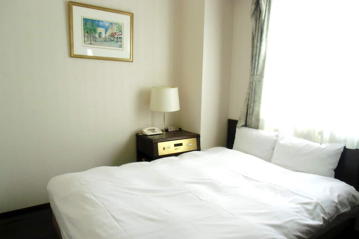 A hotel room with a neatly made bed, a bedside table with a lamp, a phone, and a framed picture on the wall.