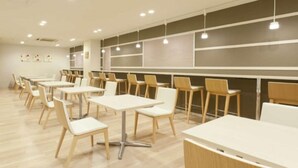 A modern dining area with white tables and chairs, recessed lighting, and a neutral color scheme. - Hotel Green With (Sendai)