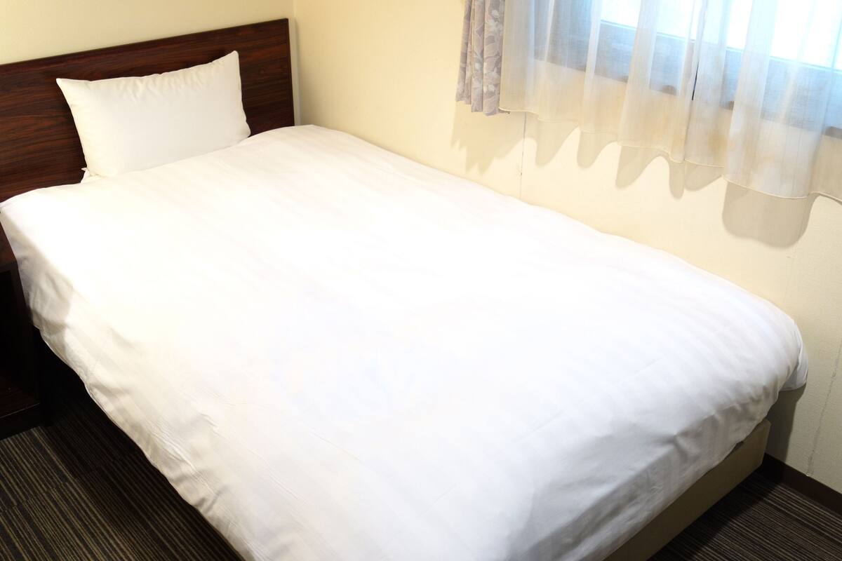 A single bed with white bedding in a room with a wooden headboard.
