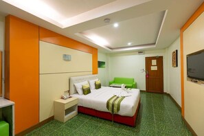 Una habitación de hotel con cama, sofá verde, televisión y escritorio con teléfono.