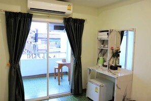A room with a sliding glass door to a balcony, a small table with a chair, a refrigerator, and a mirror with shelves above. - Lucky Green View (Bangkok)