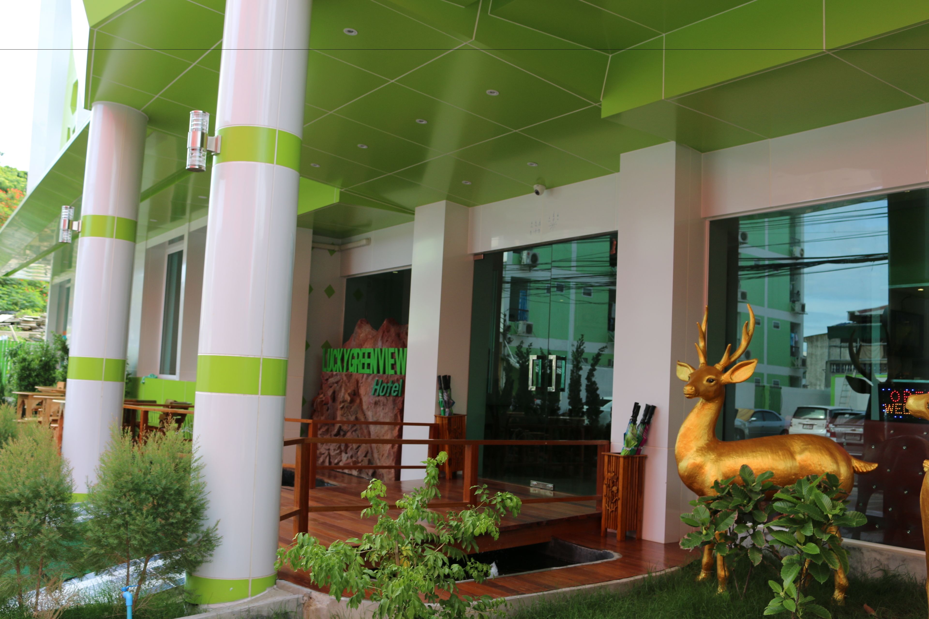 A hotel entrance with green and white pillars, a wooden bench, and a deer statue.