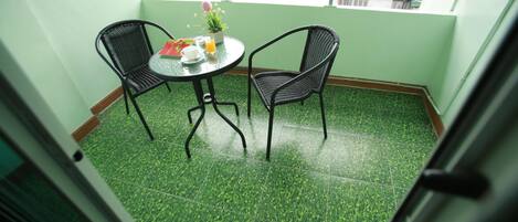 Un balcon doté d’un sol recouvert d’un gazon artificiel vert, de deux fauteuils en osier, d’une petite table ronde ornée d’une plante en pot et d’un verre de jus d’orange.
