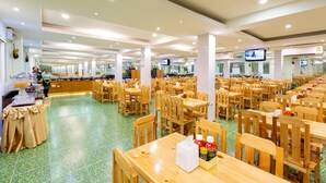 Una amplia cafetería con varias mesas y sillas de madera, una zona de bufé y una pantalla de televisión.