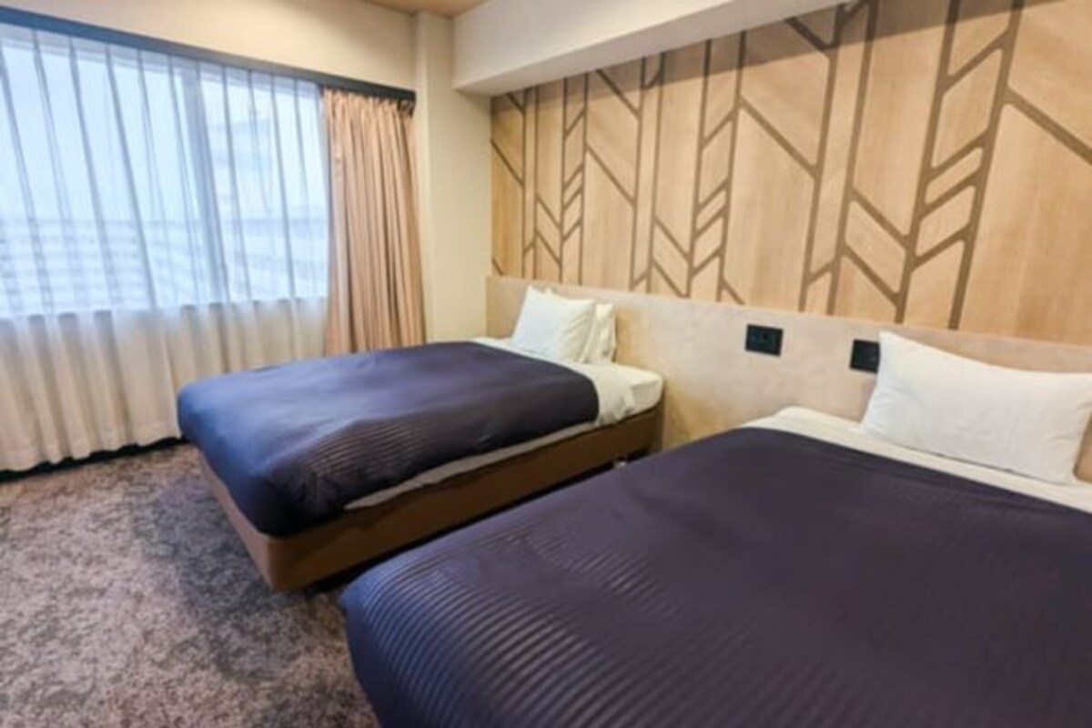 A hotel room with two beds, a large window with curtains, and a geometric-patterned headboard.