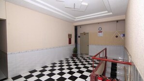 A hallway with a black and white checkered floor, a red railing, and a door in the background.