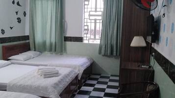 Une chambre d’hôtel avec trois lits, un sol à carreaux, une fenêtre avec des rideaux, un ventilateur de plafond et une lampe fixée au mur.
