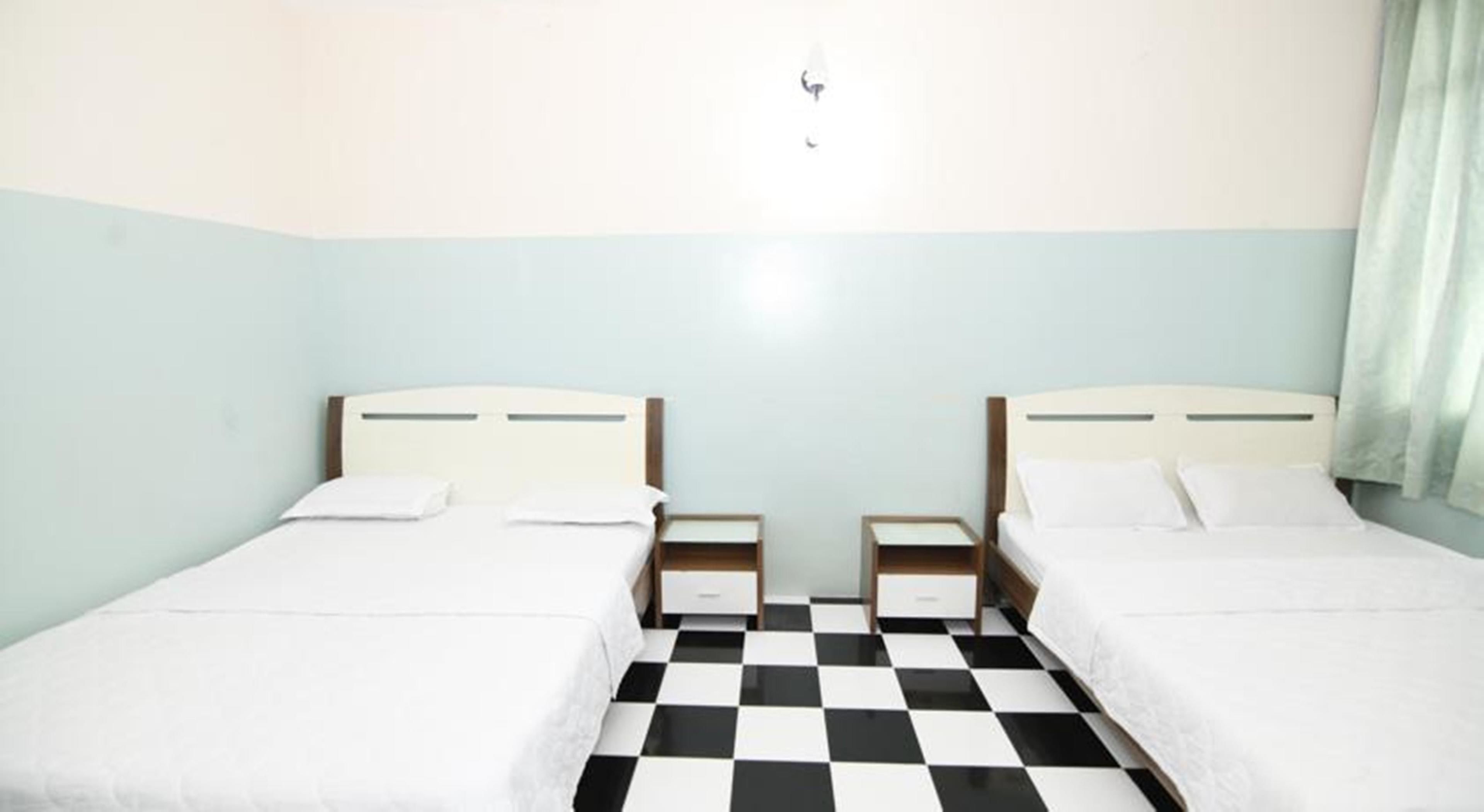 Ein Zimmer mit zwei Betten, jeweils mit einem Nachttisch, einem karierten Boden und hellblauen Wänden.