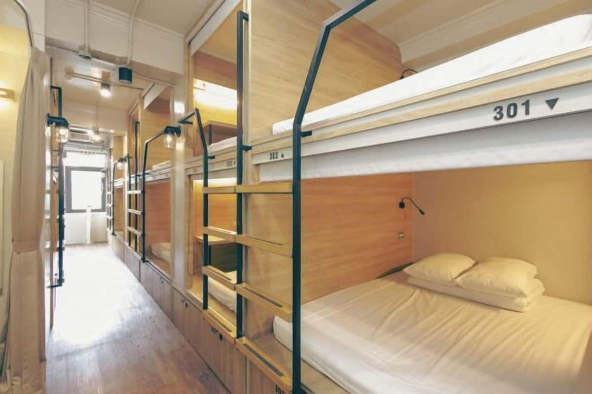 A train compartment with bunk beds, wooden paneling, and a corridor leading to a door.