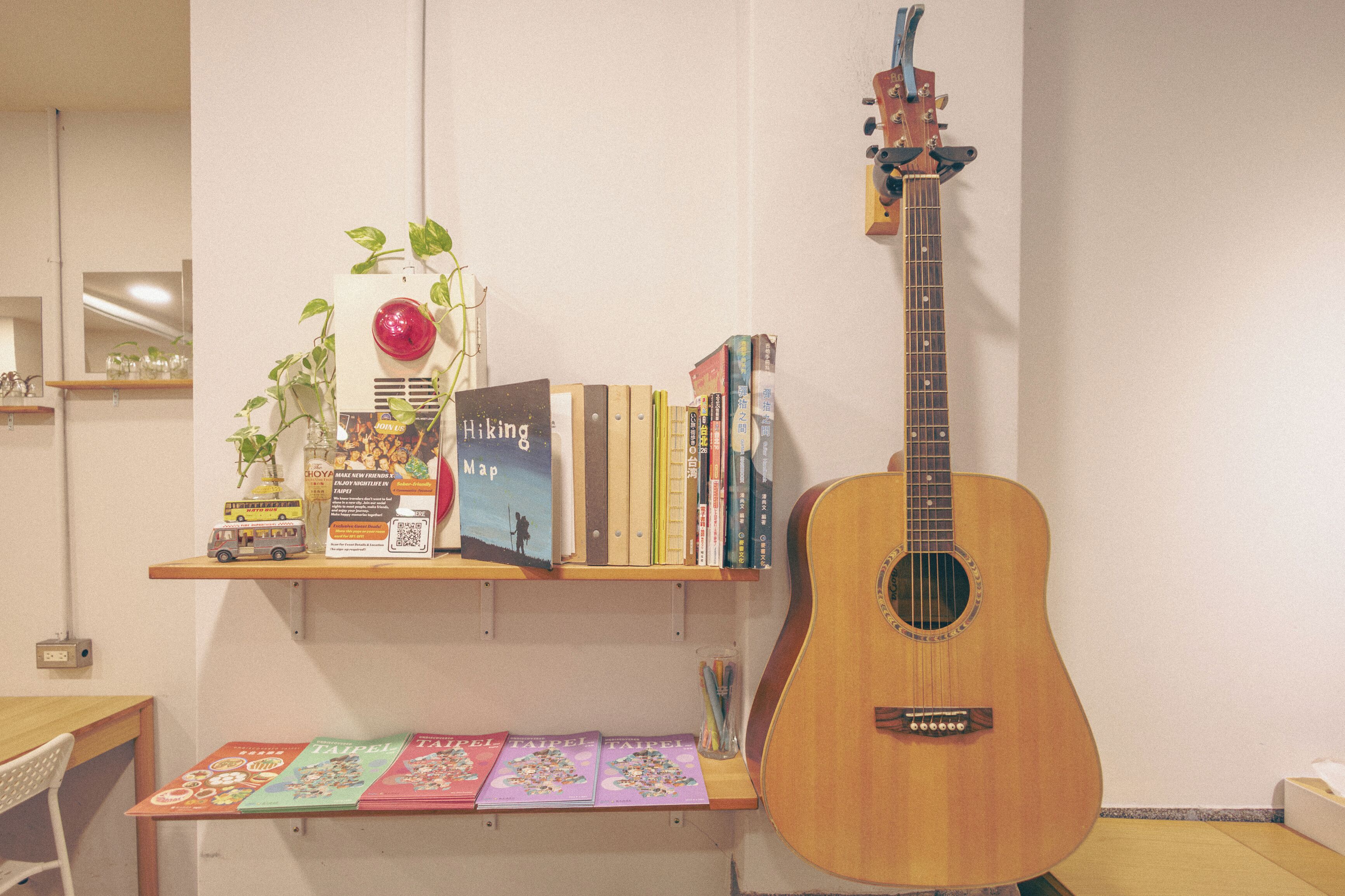A room with a guitar, bookshelves, a small table with books, and a plant.