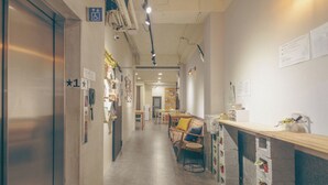 A hallway with an elevator, a reception desk, and a seating area with a patterned sofa. - DONGMEN 3 Capsule Inn - Hostel (Taipei)