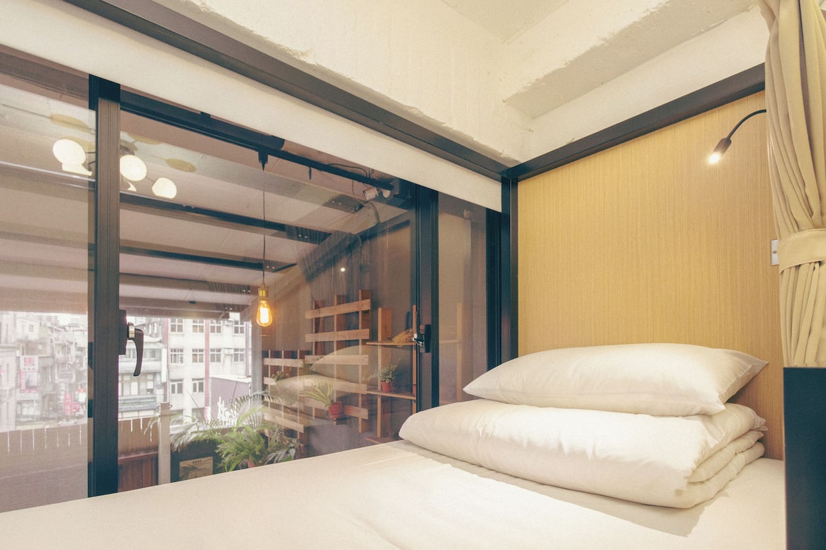 A modern bedroom with a bed, a sliding glass door, and a view of buildings outside.