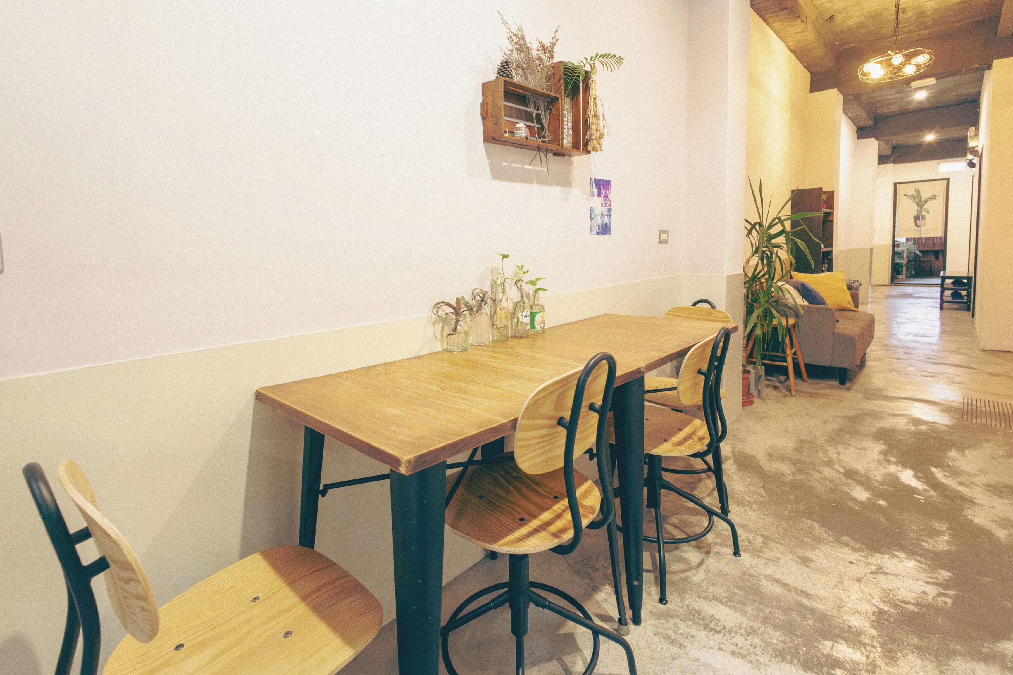 A dining area with a wooden table and chairs, a small shelf with plants, and a hallway leading to another room.