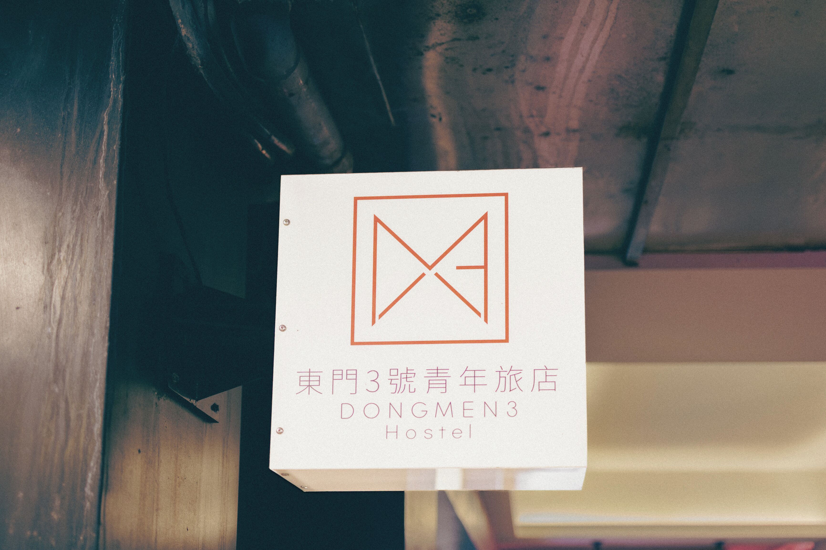 A sign with a geometric logo and text indicating 'Dongmen 3 Hostel' in both Chinese and English.