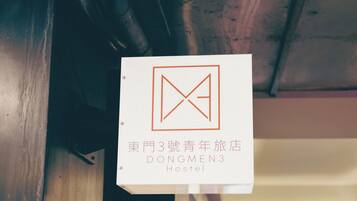 A sign with a geometric logo and text indicating 'Dongmen 3 Hostel' in both Chinese and English.